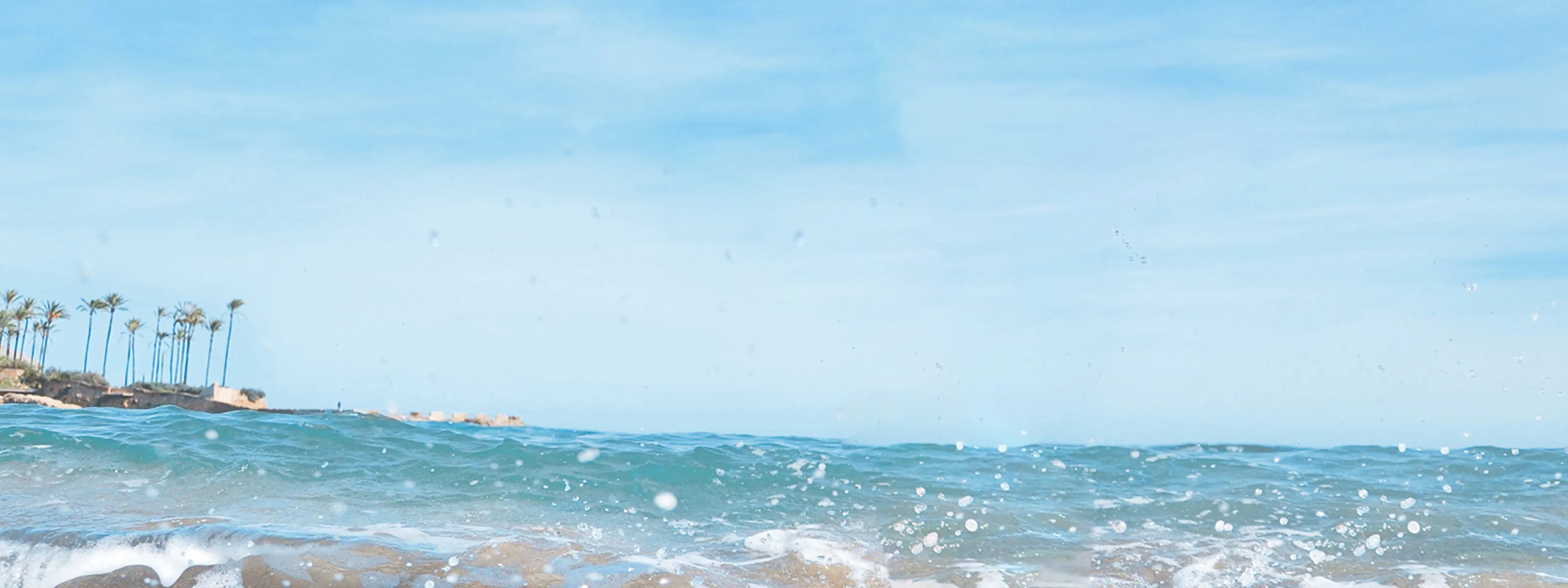 Small girl with brown hair in a pigtail on the top of her head laughing and playing in the water wearing yellow water-wings