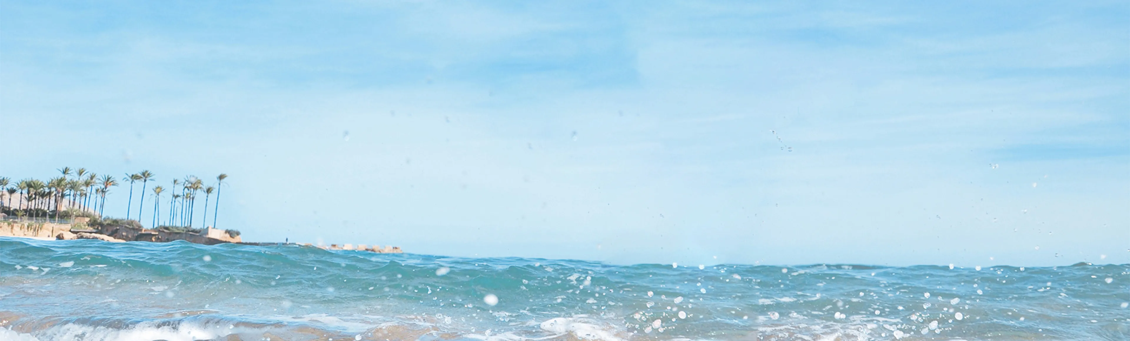 Small girl with brown hair in a pigtail on the top of her head laughing and playing in the water wearing yellow water-wings